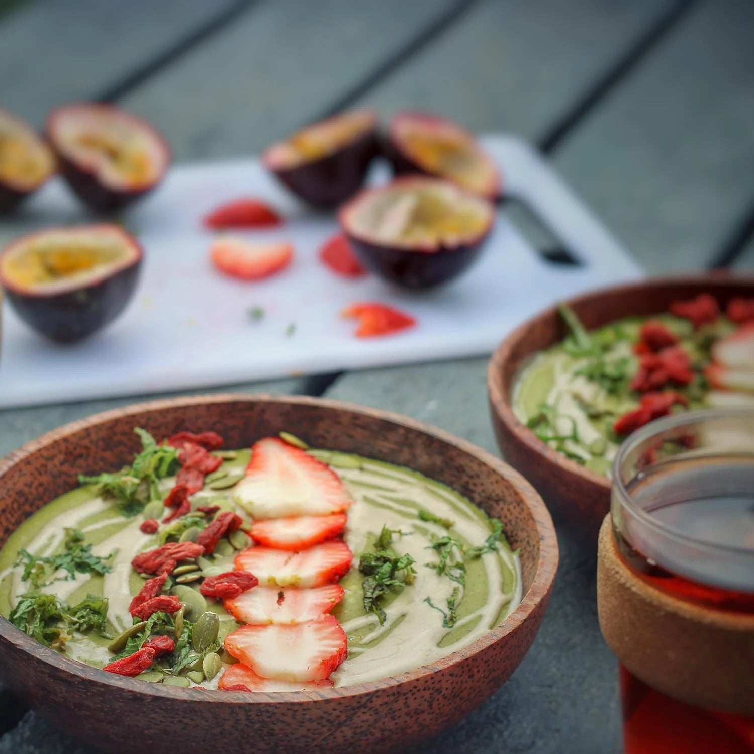 Two bowls of green smoothie with strawberries and goji berries on a wooden surface made with Wazoogles Protein Blend