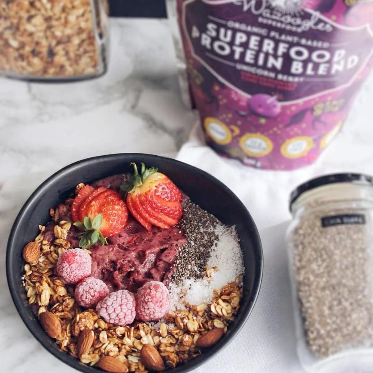 Bowl of acai bowl with granola, berries, and superfood protein blend in the background.