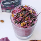 Purple smoothie with toppings in a glass, with a box of made with Wazoogles Superfood Protein Blend Unicorn Berry