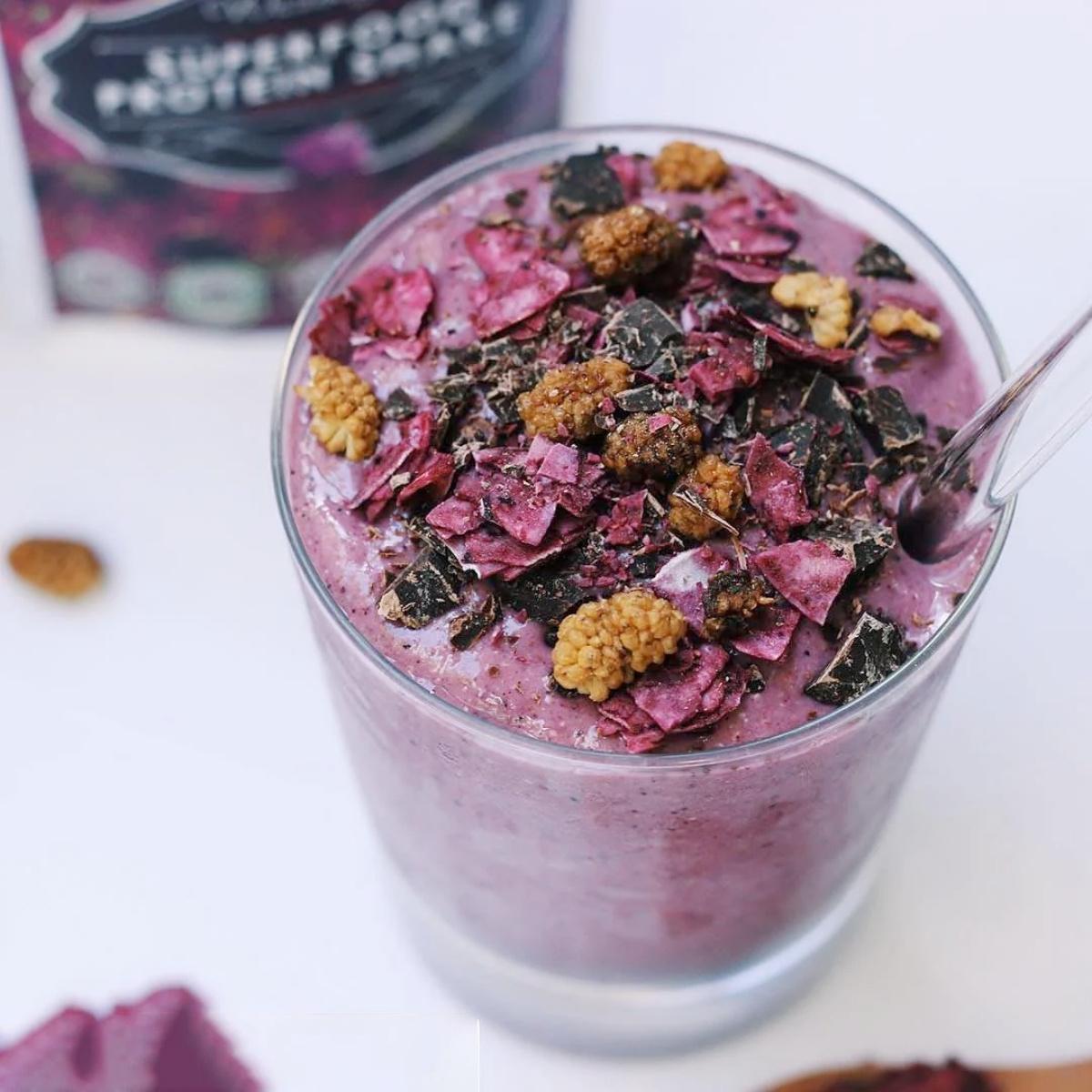 Purple smoothie with toppings in a glass, with a box of made with Wazoogles Superfood Protein Blend Unicorn Berry